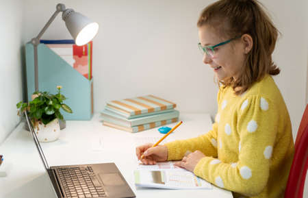 Pretty little schoolgirl is on online lesson sitting in her room during homeschoolingの写真素材