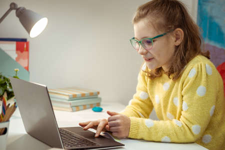 Pretty little schoolgirl is on online lesson sitting in her room during homeschoolingの写真素材