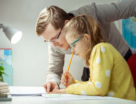 Young father teaching and helping his daughter with homework during pandemic quarantine homeschoolingの写真素材