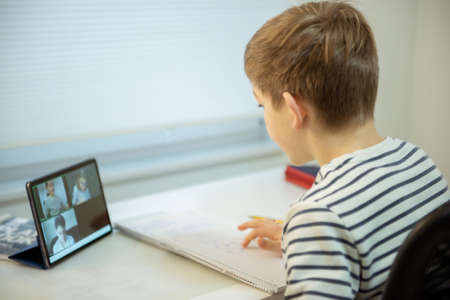 Teenager school boy having virtual lesson at home using tablet during homeschooling at pandemic quarantineの写真素材