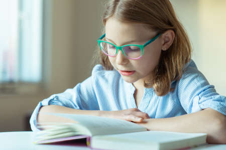 Happy pretty teen girl reading book at desk at home during pandemic distance learningの写真素材