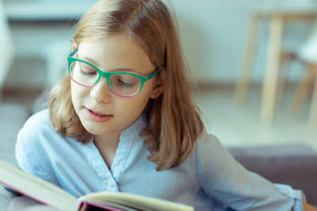 Happy pretty teen girl reading book at desk at home during pandemic distance learningの写真素材