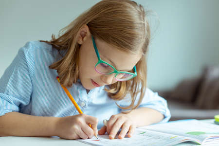 Pretty teen schoolgirl in glasses making her math homework at desk at home during pandemic distance learningの写真素材