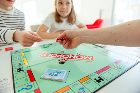 KIEL, GERMANY - February 14, 2021: Hands with money of happy children having fun playing board game in cozy family time with their parentsのeditorial素材