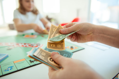 KIEL, GERMANY - February 14, 2021: Hands with money of happy children having fun playing board game in cozy family time with their parentsのeditorial素材