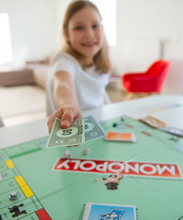 KIEL, GERMANY - 14 February 2021: Portrait of cute child girl giving money having fun playing board game in cozy family time evening together with their parentsのeditorial素材