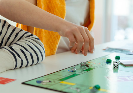 KIEL, GERMANY - February 14, 2021: Hands with money of happy children having fun playing board game in cozy family time with their parentsのeditorial素材
