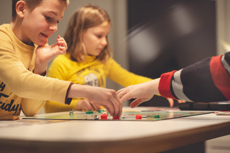 KIEL, GERMANY - 07 December 2020: Happy children having fun playing board game in cozy family time evening together with their parentsのeditorial素材