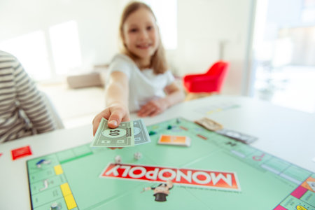 KIEL, GERMANY - 14 February 2021: Portrait of cute child girl giving money having fun playing board game in cozy family time evening together with their parentsのeditorial素材