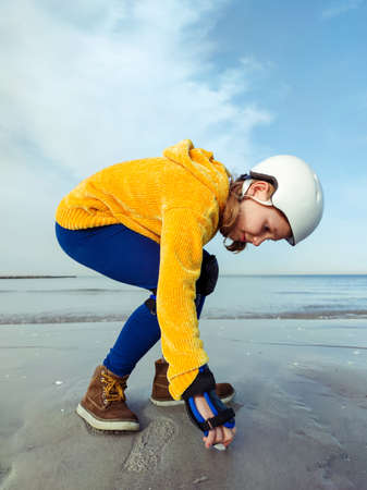 Portrait of pretty teenager child girl in yellow pullover, helmet and inline protective equipment posing on Baltic sea beachの写真素材