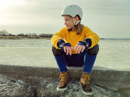 Portrait of pretty teenager child girl in yellow pullover, helmet and inline protective equipment posing on Baltic sea beachの写真素材