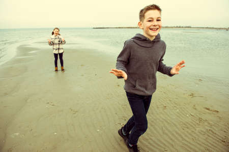 Two happy teenager children siblings walking and playing on Baltic sea beach in spring