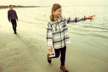 Two happy teenager children siblings walking and playing on Baltic sea beach in spring