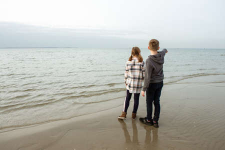 Two happy teenager children siblings walking and playing on Baltic sea beach in springの写真素材