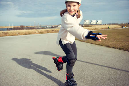 Happy teenager child girl in white helmet, inline skates and safety equipment having fun during learning skating at sunny dayの写真素材