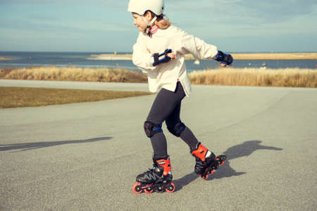 Happy teenager child girl in white helmet, inline skates and safety equipment having fun during learning skating at sunny dayの写真素材