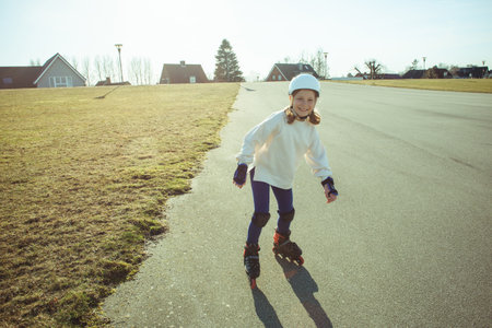 Happy teenager child girl in white helmet, inline skates and safety equipment having fun during learning skating at sunny dayの写真素材