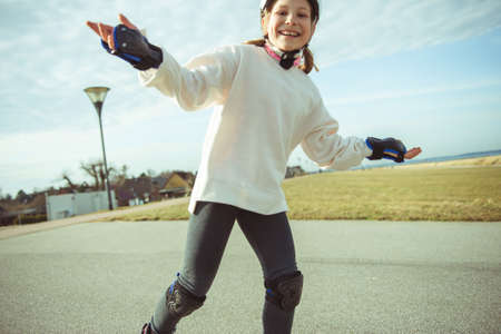Happy teenager child girl in white helmet, inline skates and safety equipment having fun during learning skating at sunny dayの写真素材