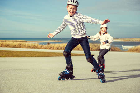 Happy siblings teenager boy and girl having fun during inline skating at sunny summer day at Baltic sea promenadeの写真素材