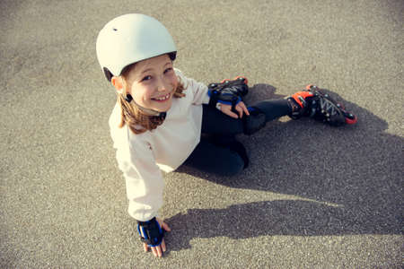 Portrait of pretty little teenager child girl sitting in white helmet, inline skates and safety equipment posingの写真素材