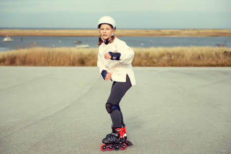Happy teenager child girl in white helmet, inline skates and safety equipment having fun during learning skating at sunny dayの写真素材