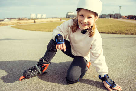 Portrait of pretty little teenager child girl sitting in white helmet, inline skates and safety equipment posingの写真素材