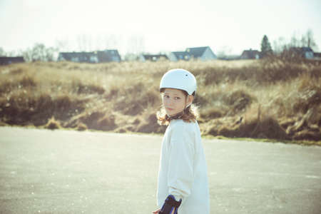 Happy teenager child girl in white helmet, inline skates and safety equipment having fun during learning skating at sunny dayの写真素材