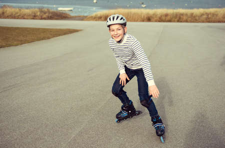 Happy teenager boy in helmet, inline skates and safety equipment is happy learning skating sunny day in summerの写真素材