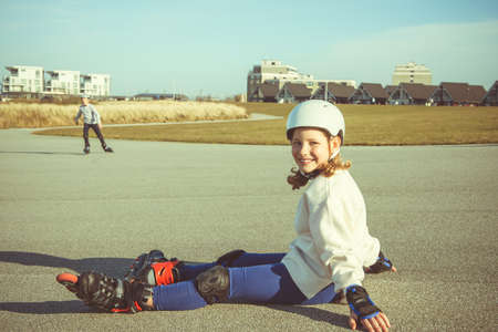 Portrait of pretty little teenager child girl sitting in white helmet, inline skates and safety equipment posingの写真素材