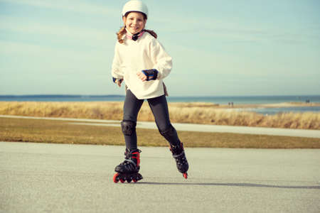 Happy teenager child girl in white helmet, inline skates and safety equipment having fun during learning skating at sunny dayの写真素材
