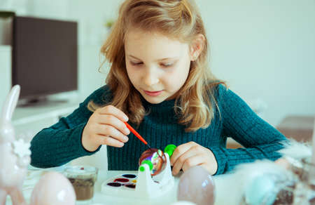 Cute little blonde girl painting Easter eggs at homeの写真素材