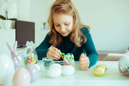 Cute little blonde girl painting Easter eggs at homeの写真素材