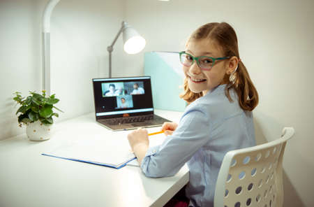 Cute little school girl having virtual lesson at home using laptop during homeschooling at pandemic quarantineの写真素材