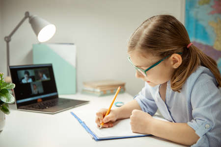 Cute little school girl having virtual lesson at home using laptop during homeschooling at pandemic quarantineの写真素材