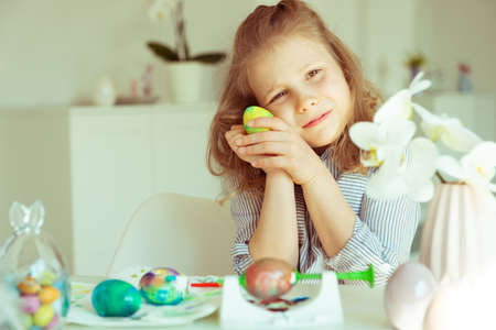 Cute little blonde girl painting Easter eggs at homeの写真素材