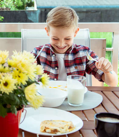 Happy little boy having fun during breakfast on the big terrasse at homeの写真素材