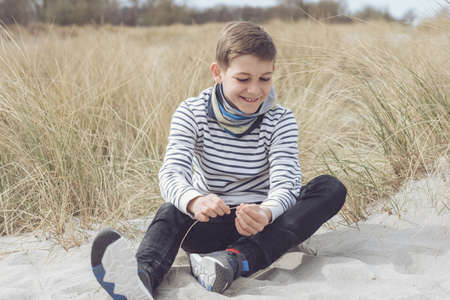 Portrait of handsome teenage boy sitting and smiling on white sand on Baltic sea beach with dunesの写真素材