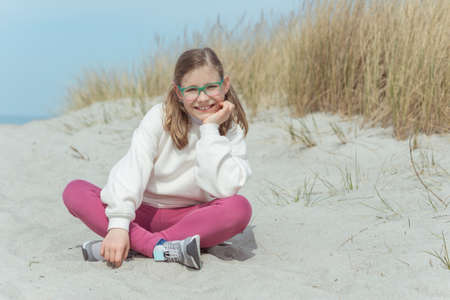 Portrait of pretty little teenage girl sitting on white sand in dunes on Baltic seaの写真素材
