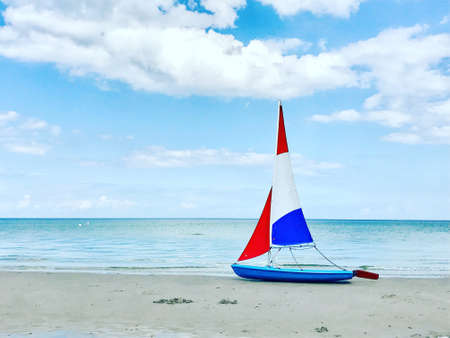Photo of little boat with colorful sails on white sand beach at cloudy weather in north Germanyの写真素材