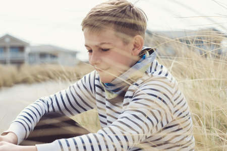 Portrait of handsome teenage boy sitting and smiling on white sand on Baltic sea beach with dunesの写真素材