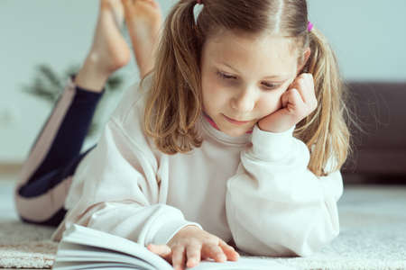 Portrait of cute teen girl reading book on floor of living room at home