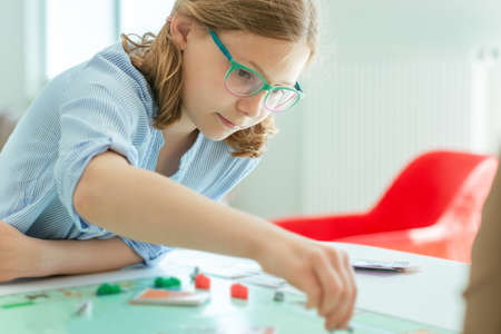 Portrait of pretty teen girl in glasses playing board game with parents at homeの写真素材