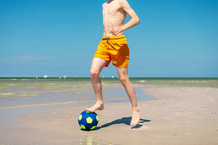 Happy teen boy playing with ball on beach at summer sunny day with blue sky on backgroundの写真素材