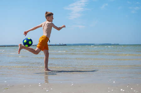Happy teen boy playing with ball on beach at summer sunny day with blue sky on backgroundの写真素材