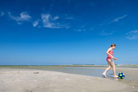 Cute little teen girl playing and having fun with ball on beach at sunny summer dayの写真素材