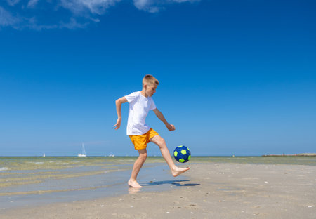 Happy teen boy playing with ball on beach at summer sunny day with blue sky on backgroundの写真素材