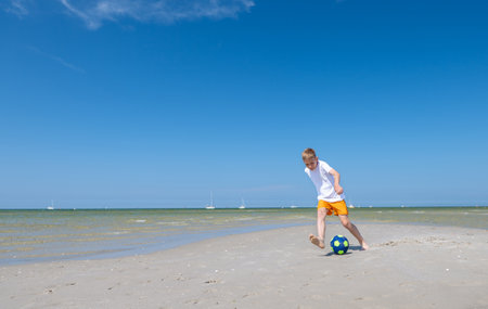 Happy teen boy playing with ball on beach at summer sunny day with blue sky on backgroundの写真素材