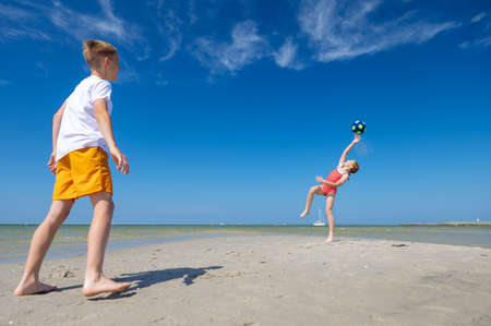 Happy children playing with ball on beach at summer sunny day with blue sky on backgroundの写真素材