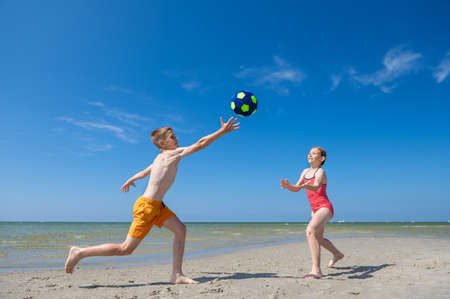 Happy children playing with ball on beach at summer sunny day with blue sky on backgroundの写真素材