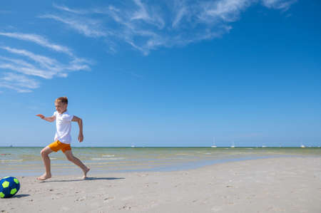 Happy teen boy playing with ball on beach at summer sunny day with blue sky on backgroundの写真素材
